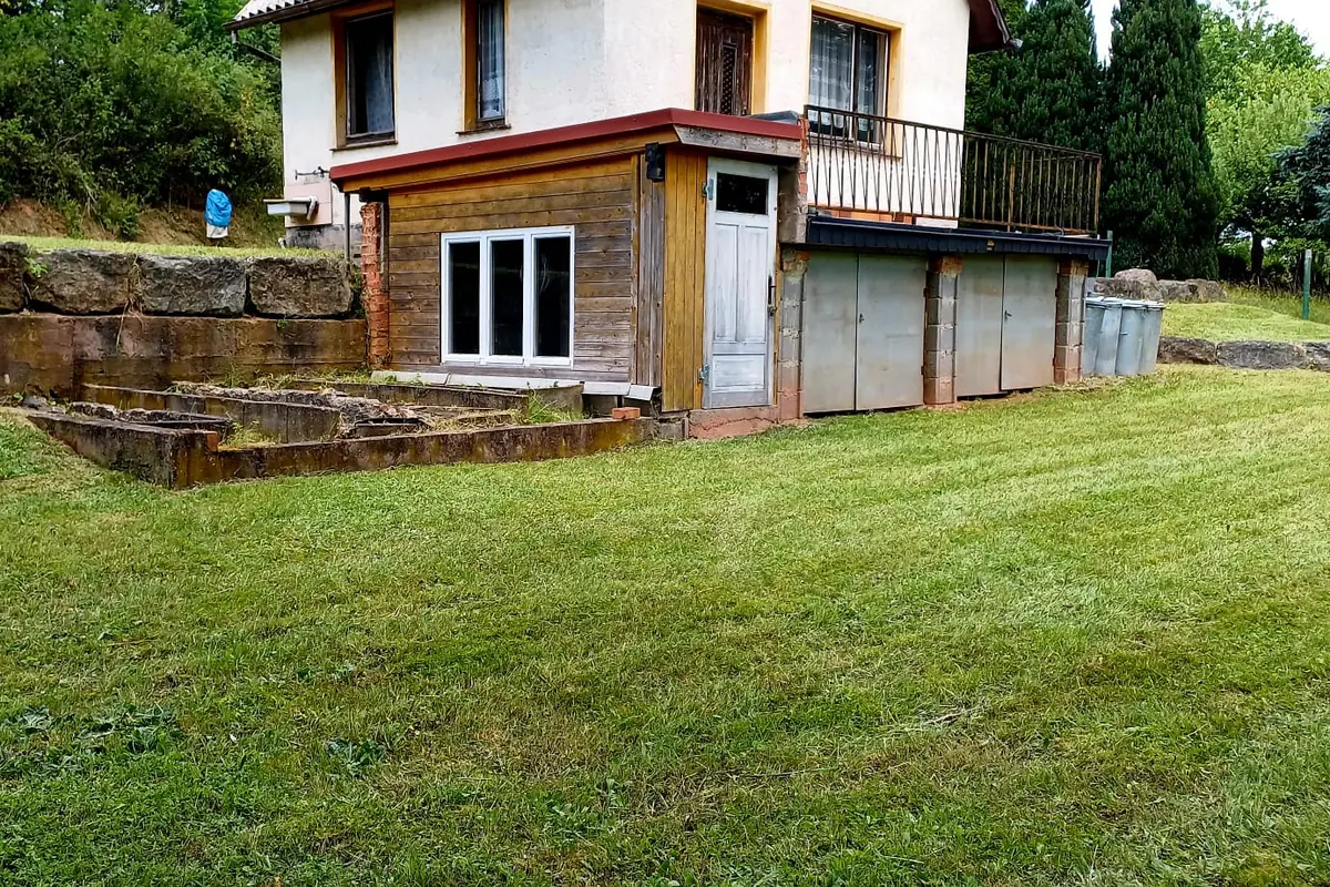 Gepflegtes Hanggrundstück mit Natursteinmauer und Wohnhaus nach der Mahd